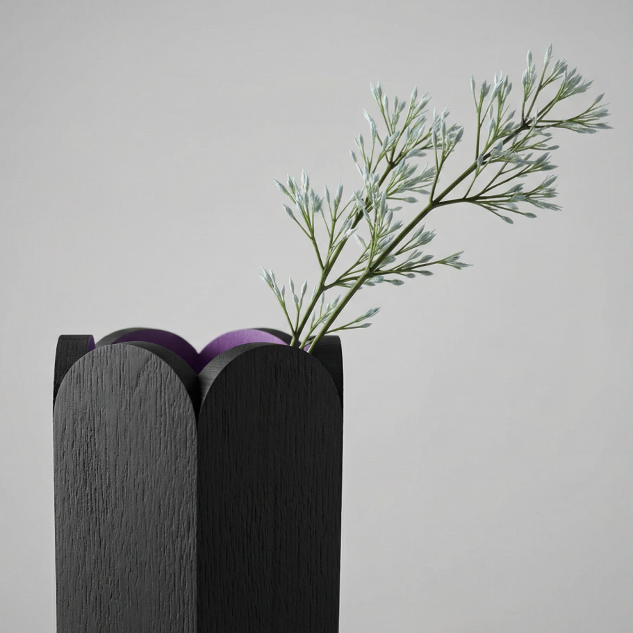 Schwarze Vase mit zwei lila Kugeln und einem grünen Zweig.